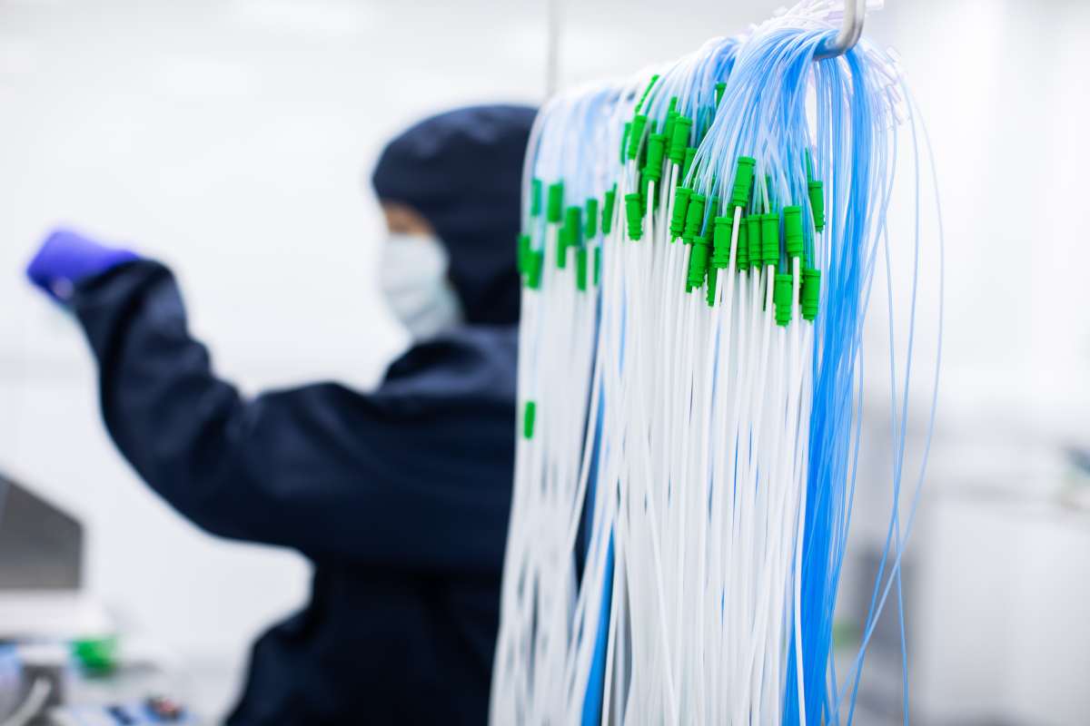 Cleanroom operator assembling blue and white medical tubing with green connectors for single-use urology devices at Meridian Medical.